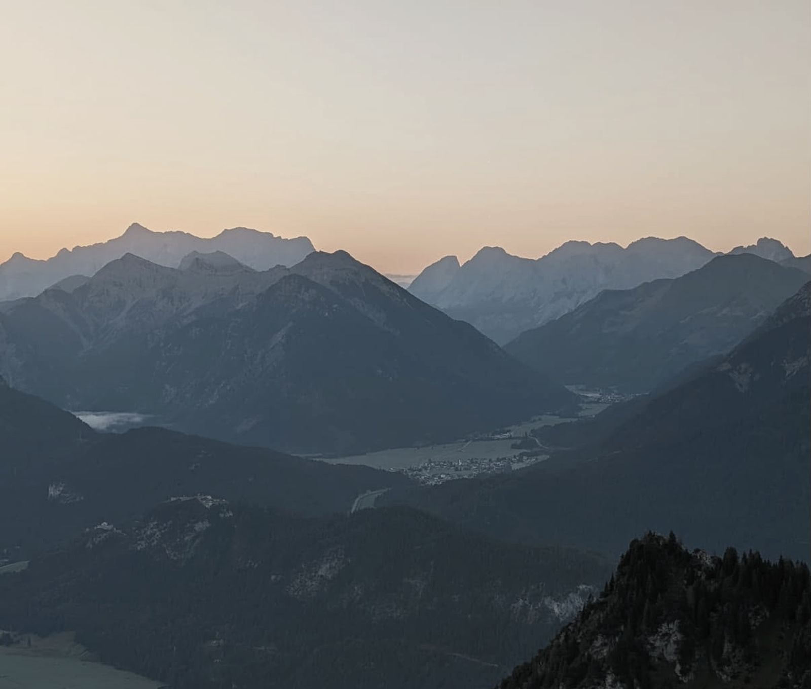 Bergkette in der Abenddämmerung, davor bewaldete Hänge.