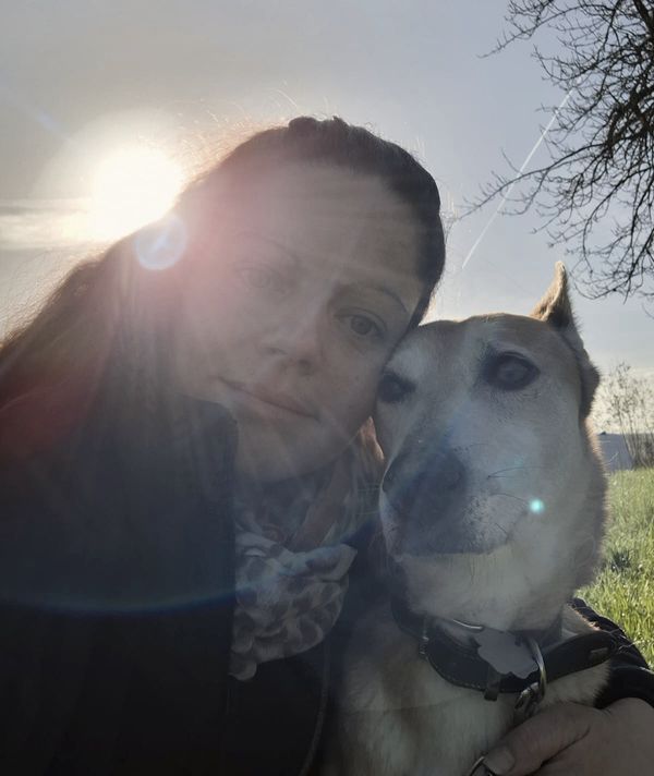 Katja Kalkau lehnt ihren Kopf an ihren Hund, im Gegenlicht der tiefstehenden Sonne.